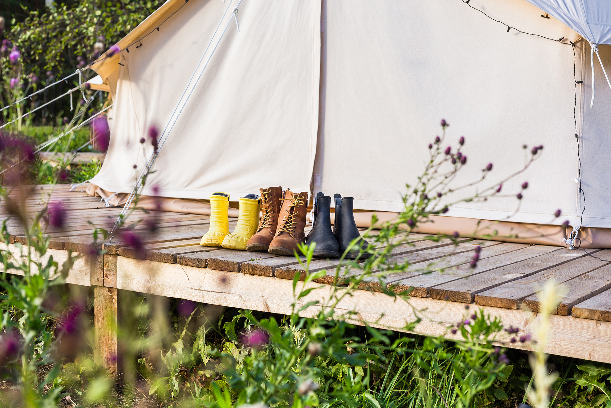 Bell tent with decking with a row of outdoor boots and bright yellow wellies lined up in front of the tent entrance